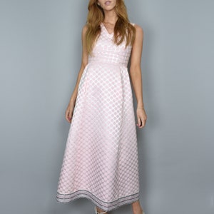 Puede incluir: Una mujer lleva un vestido maxi rosa sin mangas con lunares blancos y ribete plateado. El vestido tiene un corpiño ajustado y una falda fluida.