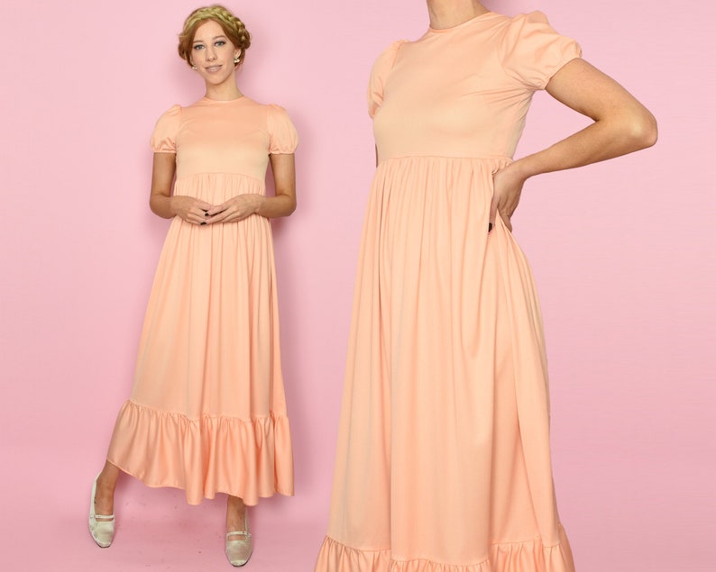 May include: A peach-colored maxi dress with short puff sleeves and a gathered skirt. The dress has a simple, classic design and is perfect for a summer occasion.