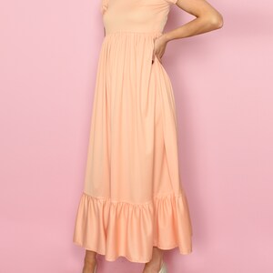 May include: A peach-colored maxi dress with a gathered waist and a ruffled hem. The dress has short puff sleeves and a round neckline.