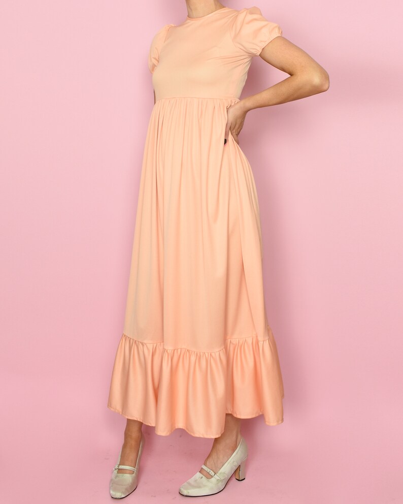 May include: A peach-colored maxi dress with a gathered waist and a ruffled hem. The dress has short puff sleeves and a round neckline.