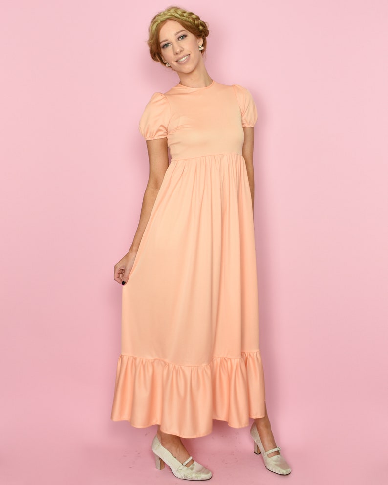 May include: A peach-colored maxi dress with a ruffled hem and short puff sleeves. The dress has a fitted bodice and a flowy skirt.