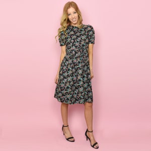 May include: A woman wearing a black midi dress with a floral print. The dress has a round neckline and short sleeves. She is wearing black heeled sandals.