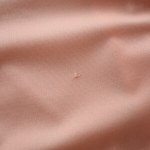 May include: Close-up of a peach-colored fabric with a small hole in the center.