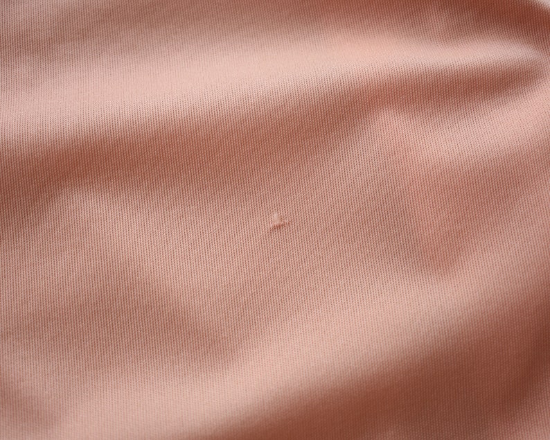 May include: Close-up of a peach-colored fabric with a small hole in the center.