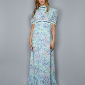 May include: A long, white maxi dress with a blue and green floral print. The dress has a high neck, short sleeves, and a ruffled hem.