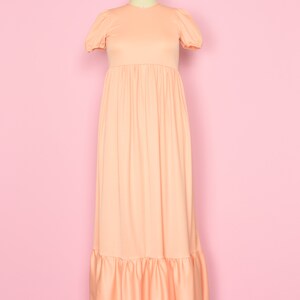May include: A peach-colored maxi dress with a round neckline and short puff sleeves. The dress has a gathered waist and a tiered ruffle hem.