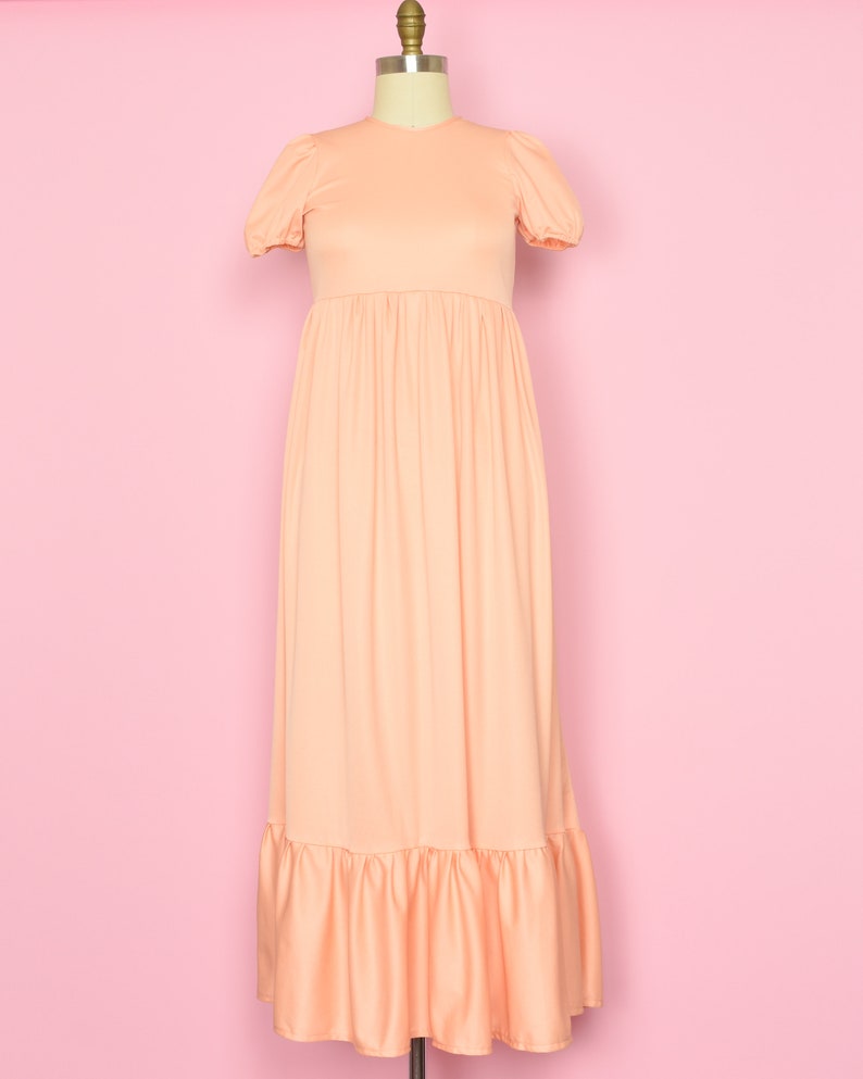 May include: A peach-colored maxi dress with a round neckline and short puff sleeves. The dress has a gathered waist and a tiered ruffle hem.