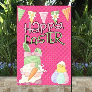 K&ouml;nnte beinhalten: Eine rosa Gartenflagge mit einem wei&szlig;en und gr&uuml;nen Zwerg, der eine Karotte h&auml;lt, einem gelben K&uuml;ken mit drei pastellfarbenen Eiern und dem Text "Frohe Ostern" in rosa und gr&uuml;nen Buchstaben.
