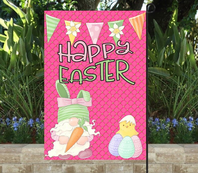K&ouml;nnte beinhalten: Eine rosa Gartenflagge mit einem wei&szlig;en und gr&uuml;nen Zwerg, der eine Karotte h&auml;lt, einem gelben K&uuml;ken mit drei pastellfarbenen Eiern und dem Text "Frohe Ostern" in rosa und gr&uuml;nen Buchstaben.