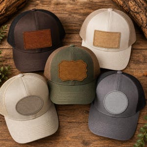 May include: A collection of five trucker hats in various colors, including brown, olive green, and gray. Each hat features a mesh back and a leather patch on the front. The hats are displayed on a wooden surface.
