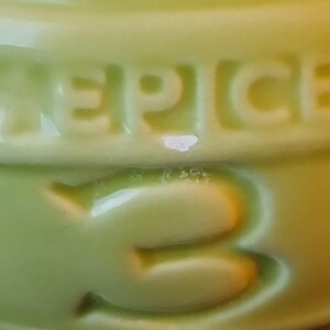 Puede incluir: Primer plano de un recipiente de cer&aacute;mica verde claro con la palabra "SPICE" en relieve en la parte superior. Debajo de la palabra "SPICE" est&aacute; el n&uacute;mero "3" en relieve en el recipiente. El recipiente tiene un acabado brillante.