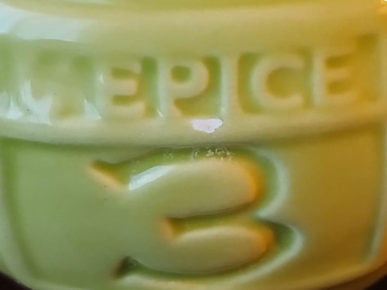 Puede incluir: Primer plano de un recipiente de cer&aacute;mica verde claro con la palabra "SPICE" en relieve en la parte superior. Debajo de la palabra "SPICE" est&aacute; el n&uacute;mero "3" en relieve en el recipiente. El recipiente tiene un acabado brillante.