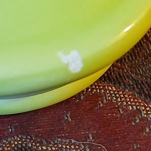 Puede incluir: Primer plano de un plato de cer&aacute;mica verde lima con borde amarillo. Una marca blanca de forma irregular es visible en la superficie del plato. El plato es parcialmente visible, lo que sugiere un conjunto o colecci&oacute;n m&aacute;s grande.