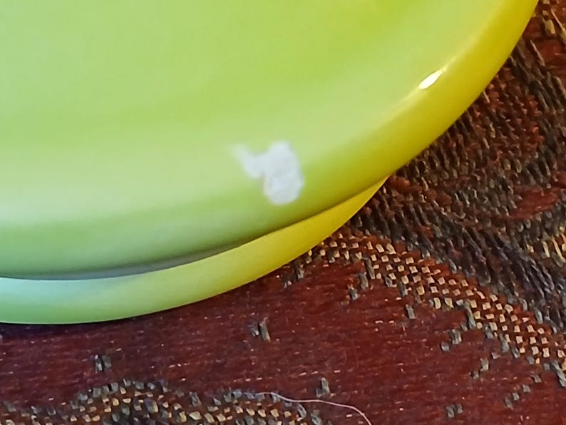 Puede incluir: Primer plano de un plato de cer&aacute;mica verde lima con borde amarillo. Una marca blanca de forma irregular es visible en la superficie del plato. El plato es parcialmente visible, lo que sugiere un conjunto o colecci&oacute;n m&aacute;s grande.