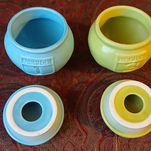 Puede incluir: Dos botes de especias de cer&aacute;mica, uno azul claro y otro verde lima, con tapas a juego. Cada bote tiene la palabra "EPICE" y un n&uacute;mero en relieve en la parte delantera. Las tapas tienen una abertura circular en el centro.