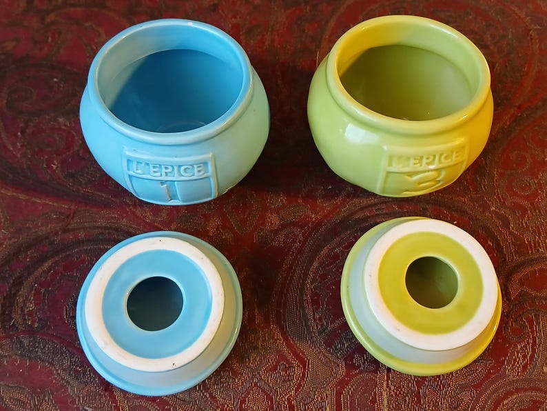 Puede incluir: Dos botes de especias de cer&aacute;mica, uno azul claro y otro verde lima, con tapas a juego. Cada bote tiene la palabra "EPICE" y un n&uacute;mero en relieve en la parte delantera. Las tapas tienen una abertura circular en el centro.