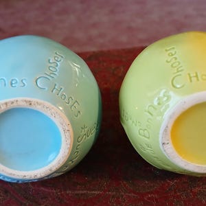 Puede incluir: Dos jarrones de cer&aacute;mica con forma de huevo, uno azul claro y otro verde amarillento, con las palabras "Bonnes Choses" en relieve en la parte superior. Los jarrones tienen una abertura circular en la parte inferior.