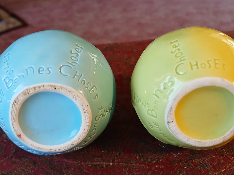 Puede incluir: Dos jarrones de cer&aacute;mica con forma de huevo, uno azul claro y otro verde amarillento, con las palabras "Bonnes Choses" en relieve en la parte superior. Los jarrones tienen una abertura circular en la parte inferior.