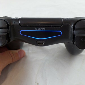 May include: A black Sony PlayStation 4 controller with a blue light bar. The controller has buttons labeled R1, R2, Share, and Options.