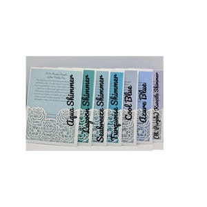 May include: Seven different color swatches of cardstock paper with a white lace overlay. The colors are aqua shimmer, lagoon shimmer, seabreeze shimmer, turquoise shimmer, cool blue, azure blue, and light purple kunzite shimmer.