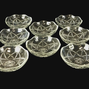 Puede incluir: Un conjunto de ocho cuencos de vidrio transparente con borde festoneado y diseño de estrella. Los cuencos están dispuestos sobre un fondo negro. Cada cuenco tiene un diámetro de aproximadamente 12,7 cm.
