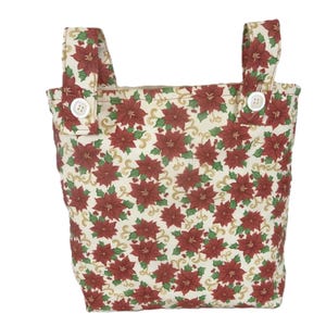 May include: A fabric tote bag with a festive poinsettia pattern. The bag features a cream background with red poinsettias, green leaves, and gold swirls. It has two handles and is secured with buttons.