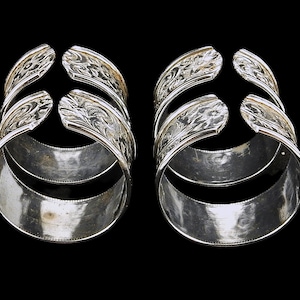 May include: Two silver, decorative, open-ended rings with intricate floral designs. The rings are stacked on top of each other.