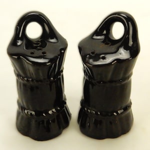 May include: A pair of black ceramic salt and pepper shakers shaped like sacks of grain. The shakers have a rope-like design around the middle and a loop at the top.