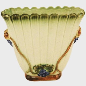 Pode incluir: Vaso de cerâmica creme com design canelado e borda ondulada. Apresenta detalhes de videira marrom, cachos de uvas azuis e detalhes florais. A borda é verde e a base marrom.