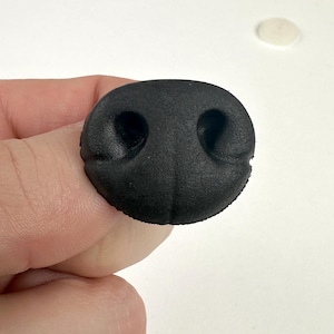 Könnte beinhalten: Schwarze Schaumstoffnase mit zwei Löchern für Nasenlöcher. Dies ist ein Bastelzubehör für die Herstellung von Tierpuppen oder anderen Bastelarbeiten.