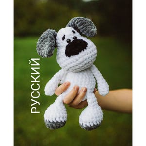 Può includere: Un giocattolo per cani in crochet bianco con orecchie grigie e un naso nero. Il giocattolo è tenuto in una mano.