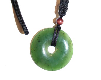 May include: A green jade pendant in the shape of a circle with a hole in the center, hanging from a black cord with a brown bead.