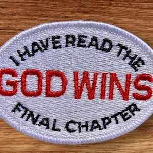 May include: Oval-shaped embroidered patch with the text "I HAVE READ THE GOD WINS FINAL CHAPTER". The text "GOD WINS" is in red, while the other text is in black. The patch is white with a stitched border.