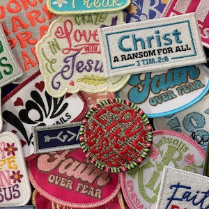 May include: A collection of assorted embroidered fabric patches featuring various religious and inspirational phrases, including Christ A RANSOM FOR ALL 1 TIM 2:6, Grace Wins, Faith Over Fear, and All My Hope Is In Jesus, in diverse shapes and colors.