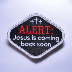 May include: A black patch with a white stitched border and the text "ALERT: Jesus is coming back soon" in red and white. Three white crosses are at the top of the patch.