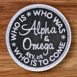 May include: A round, black patch with white embroidered text. The text reads "WHO IS * WHO WAS * WHO IS TO COME" around the edge, and "Alpha & Omega" in the center. The text "REV. 1:8" is also present. The patch has a white stitched border.
