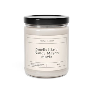 Puede incluir: Un tarro de vela blanco con tapa negra y una etiqueta que dice "MOSTLY MINDSET Smells like a Nancy Meyers movie NATURAL SOY WAX BLEND CANDLE 9 OZ".