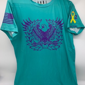 May include: Teal blue short-sleeved t-shirt with a purple eagle graphic and the text "The Quiet Professionals" on the front. The shirt also features a purple American flag on the left sleeve and a yellow ribbon with the number "22" and the text "Est. 1918" on the right sleeve.