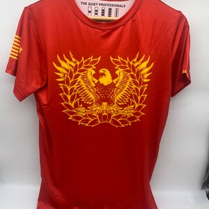 May include: Red short-sleeved t-shirt with a yellow eagle graphic and the text "THE QUIET PROFESSIONALS" on the front.