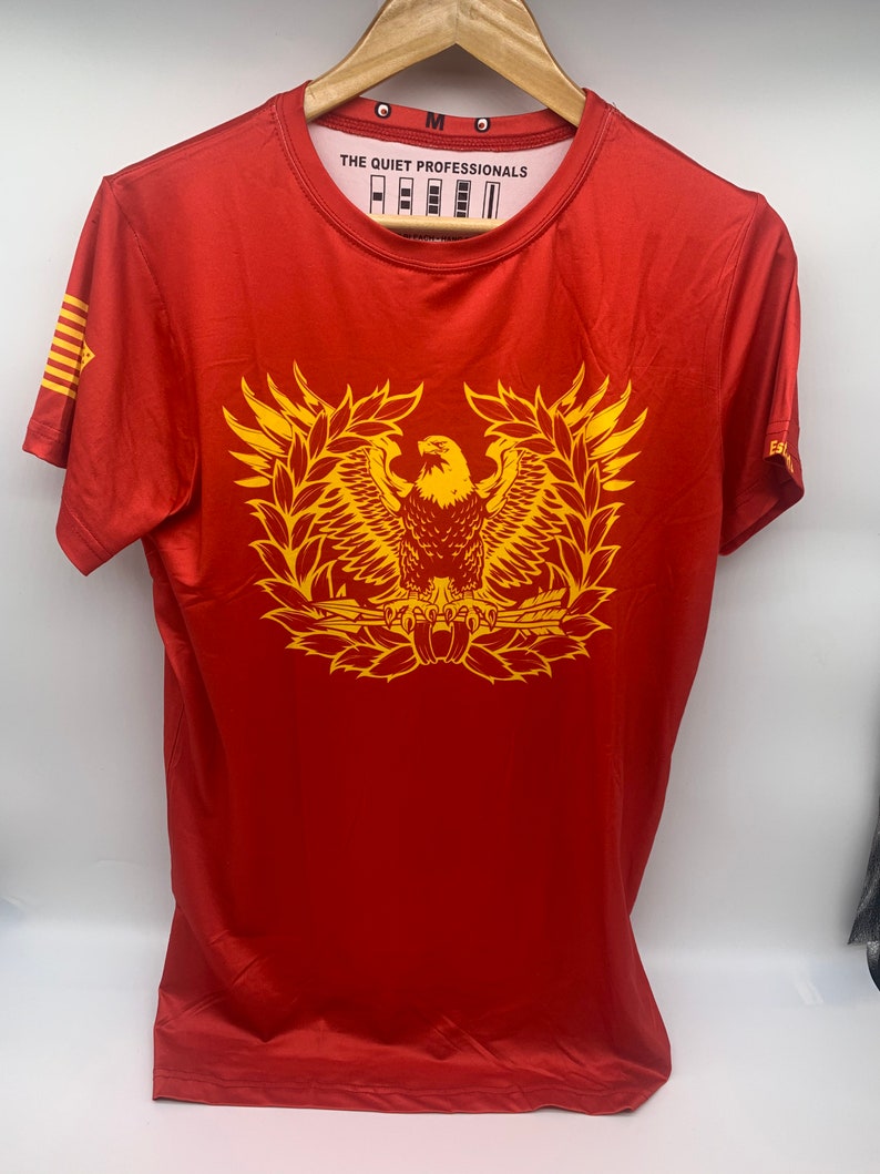 May include: Red short-sleeved t-shirt with a yellow eagle graphic and the text "THE QUIET PROFESSIONALS" on the front.