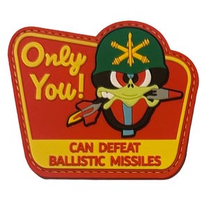 May include: A red, yellow, and green patch featuring a cartoon character in a military helmet, holding a missile. The text reads "Only You! CAN DEFEAT BALLISTIC MISSILES."