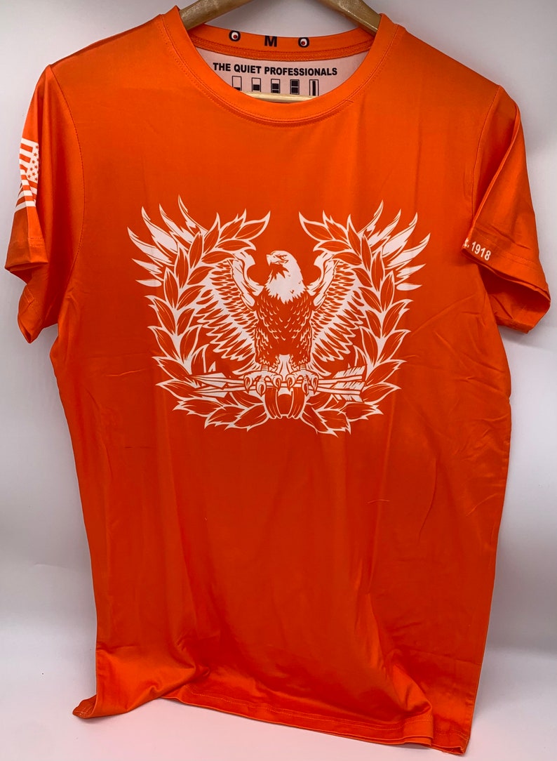 May include: Orange short-sleeved t-shirt with a white eagle graphic and the text "THE QUIET PROFESSIONALS" and "1918" printed on the shirt.