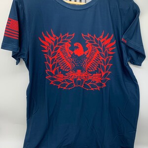 May include: A navy blue t-shirt with a red eagle graphic. The eagle is holding a rifle and is surrounded by a wreath. The text "THE QUIET PROFESSIONALS" is printed on the shirt.