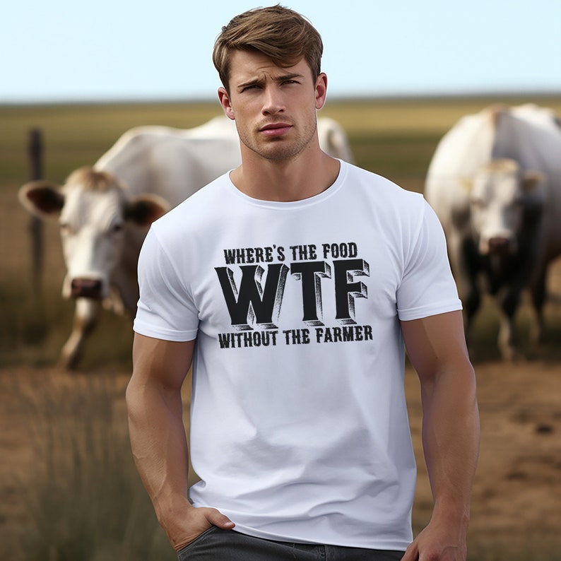 K&ouml;nnte beinhalten: Wei&szlig;es T-Shirt mit dem schwarzen Text "WHERE'S THE FOOD WTF WITHOUT THE FARMER". Die Person tr&auml;gt das Shirt vor einem verschwommenen Hintergrund mit K&uuml;hen und einem Feld.