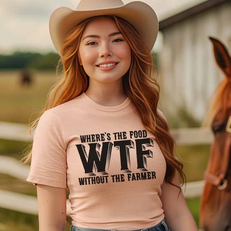 K&ouml;nnte beinhalten: Hellpfirsichfarbenes T-Shirt mit dem Text "WHERE'S THE FOOD WTF WITHOUT THE FARMER" in Schwarz. Die Person im Bild tr&auml;gt einen Cowboyhut und l&auml;chelt. Im Hintergrund ist ein Pferd zu sehen, in der N&auml;he eines Holzzauns.