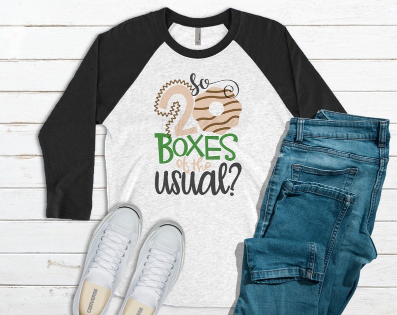 May include: A white and gray raglan shirt with black sleeves, featuring the text "So 20 Boxes of the usual?" in a playful font. The design includes donut graphics. The image also shows blue jeans and white sneakers.