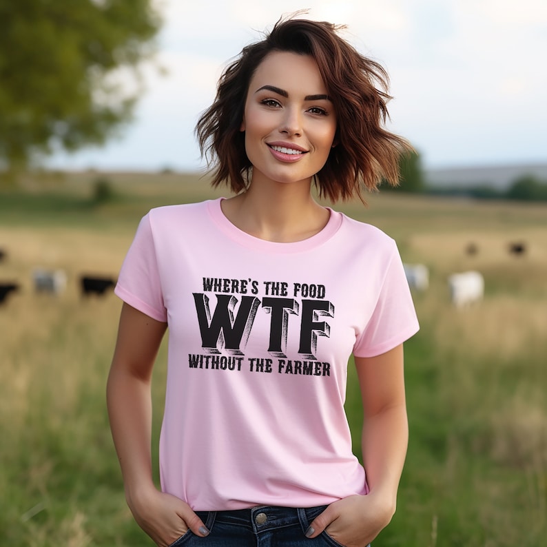 K&ouml;nnte beinhalten: Hellrosa T-Shirt mit schwarzem Text: "WHERE'S THE FOOD WTF WITHOUT THE FARMER". Das Shirt hat einen Rundhalsausschnitt. Im Hintergrund eine Weide mit K&uuml;hen.