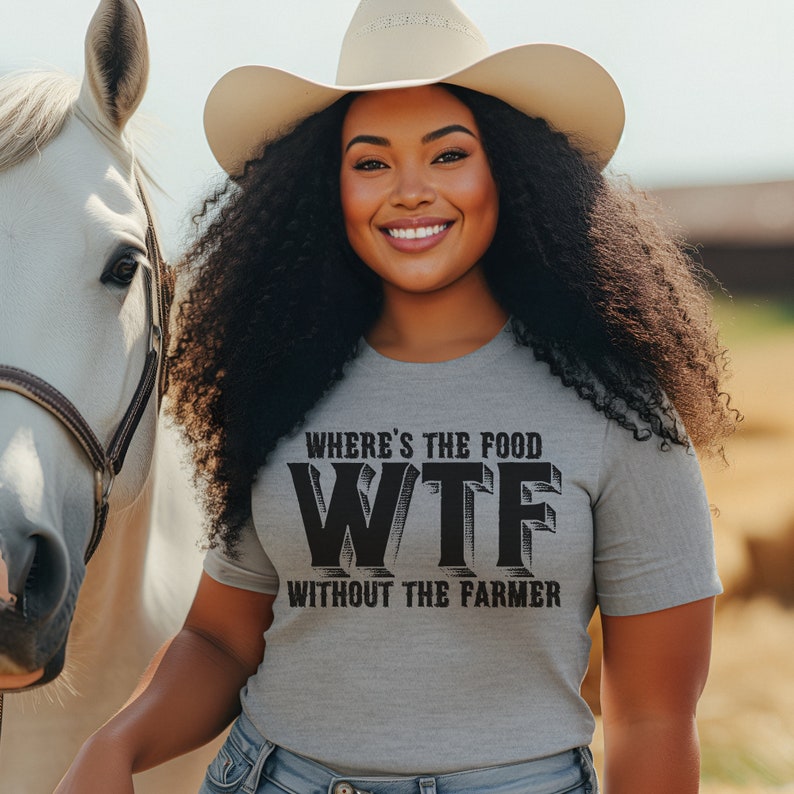 K&ouml;nnte beinhalten: Hellgraues T-Shirt mit dem schwarzen Text "WHERE'S THE FOOD WTF WITHOUT THE FARMER". Die Person tr&auml;gt einen Cowboyhut und l&auml;chelt, im Hintergrund ist ein wei&szlig;es Pferd zu sehen.