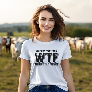K&ouml;nnte beinhalten: Ein wei&szlig;es T-Shirt mit dem schwarzen Text "WHERE'S THE FOOD WTF WITHOUT THE FARMER". Die Person, die das T-Shirt tr&auml;gt, steht vor einer Wiese mit K&uuml;hen und einer verschwommenen Landschaft.