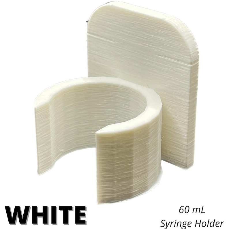 May include: A white 60 mL syringe holder featuring a vertical flat back panel and a circular, open-front clip designed to secure a syringe. The object has a visible layered texture consistent with 3D printing and includes the text WHITE 60 mL Syringe Holder.